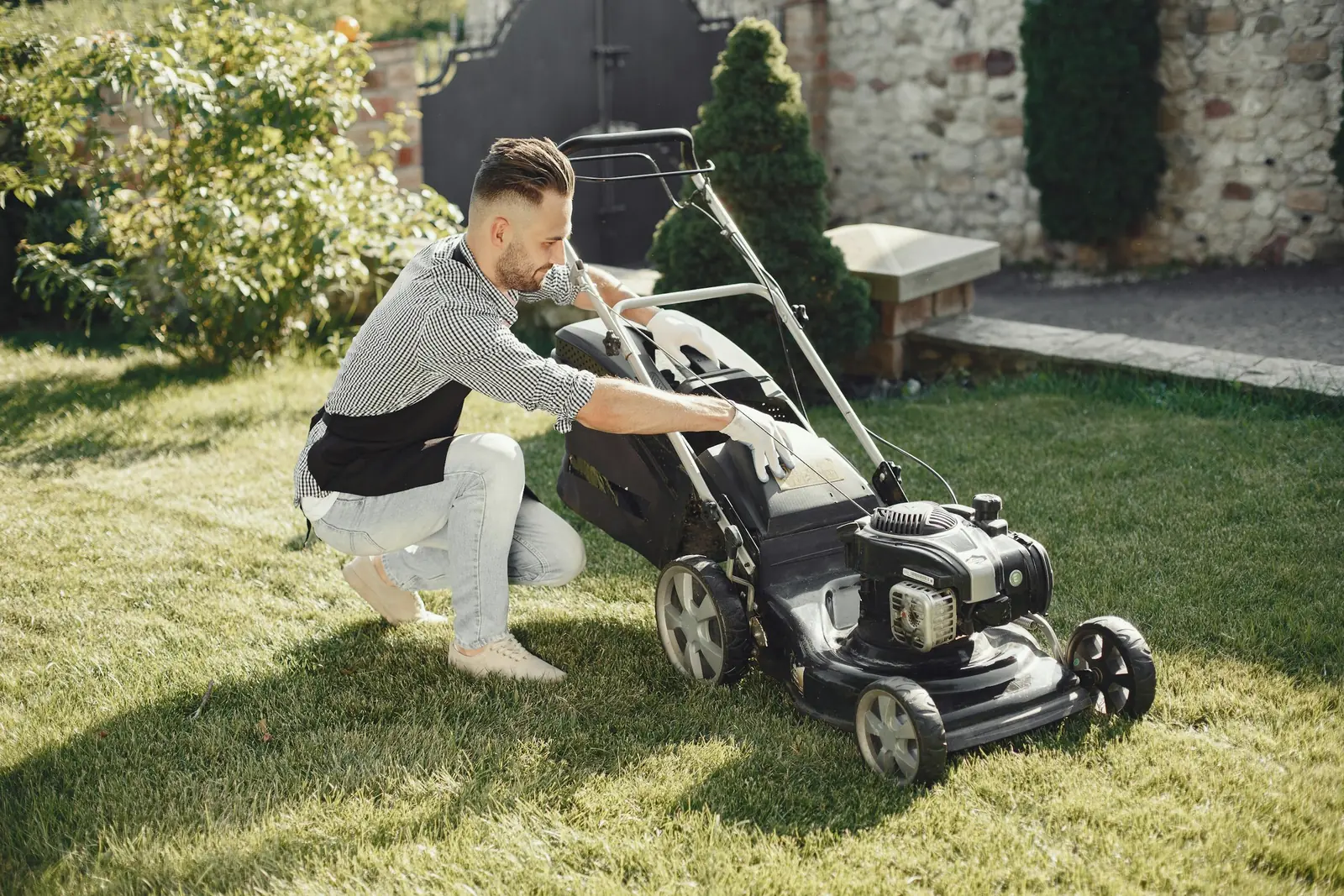 Crew member preparing a push mower on a residential lawn
